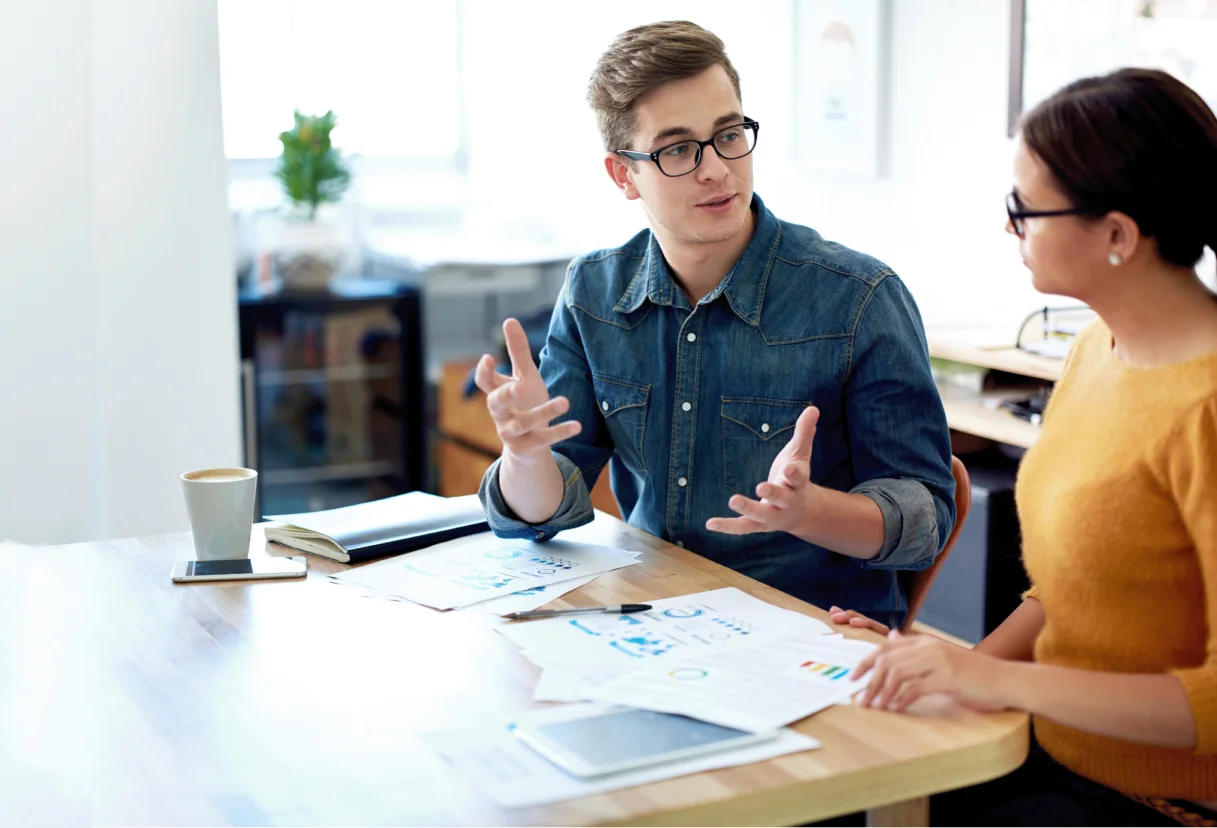 Two colleagues discussing work at table.